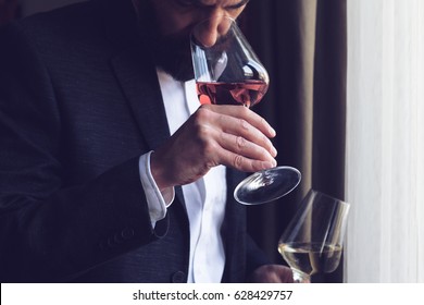 Horizontal Close Up Of A Caucasian Man With Beard Black Suit And White Shirt Tasting A Glass Of Rose Wine At An Event By The Window Natural Light