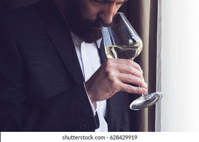 Horizontal Close Up Of A Caucasian Man With Beard Black Suit And White Shirt Tasting A Glass Of White Wine By The Window Natural Lighting