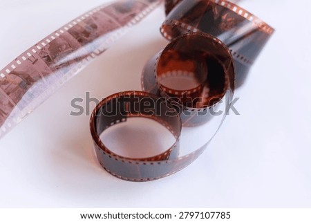 Horizontal close up of developed 35mm camera film negative rolls on a clean white surface with selective focus. Concept of analog retro photography, vintage memories, filmmaking archive, or creative hobby. Minimalist layout with copy space.