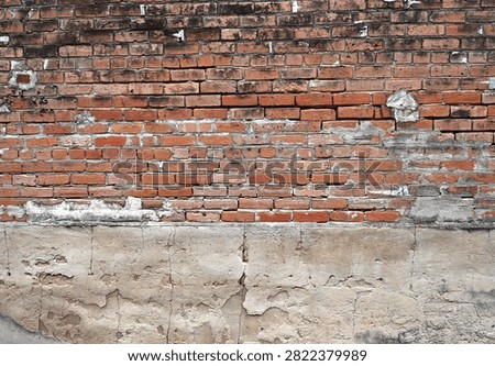A horizontal close up of a layered wall surface showing worn red bricks with cracked and uneven mortar and dark smudges on several bricks. Beneath the brick section, the concrete layer is fractured, crumbling, and exposing rough areas and deep cracks.