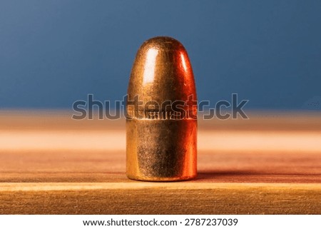 Horizontal close up shot of a copper jacketed three fifty seven caliber bullet removed from casing, standing on a wooden surface.
