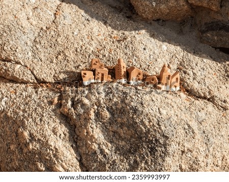 Horizontal close up shot of a set of clay miniature houses in a raw on a stone. A detail of garden decor in Sardinia, Italy
