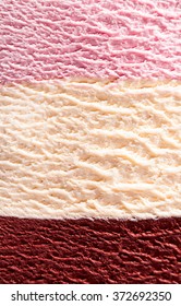 Horizontal close up of stacked strawberry, chocolate fudge and vanilla or Neapolitan flavor ice cream with delicious texture