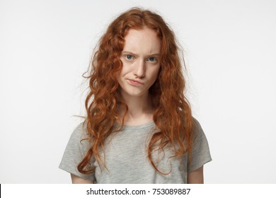 Horizontal closeup photo of teenage redhead European girl isolated on white background frowning and curling her lips showing deep mistrust and doubt as if disagreeing with what she hears or sees
