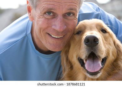 Horizontal Close-up Shot Of An Active Senior Man In Blue T-shirt Crouching Beside Golden Retriever.