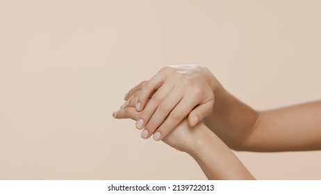 Horizontal close-up shot of female hands are rubbed and interlocked on beige background | Dry hands prevention concept