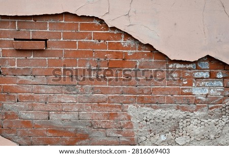 A horizontal close-up view of a deteriorating multi-layer wall surface with tan painted concrete, a cement patch with exposed metal lath, and an inner red brick layer with mortar. The tan painted concrete is scratched, cracked, and pulling away from the inner layers. The cement patch is wearing away and sluffing off, revealing the metal lath, while the red brick layer is weatherworn with a misplaced brick sticking out, discolored bricks with white and blue paint, and mortar that is worn, cracked, uneven, and missing around several bricks.