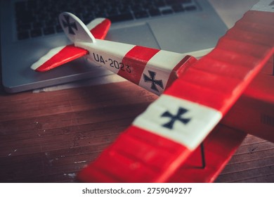 Horizontal close-up view of the tail section of a handcrafted red and white wooden triplane model, resting on a desk in a workshop.
