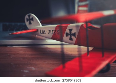 Horizontal close-up view of the tail section of a handcrafted red and white wooden triplane model, resting on a desk in a workshop.