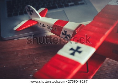 Horizontal close-up view of the tail section of a handcrafted red and white wooden triplane model, resting on a desk in a workshop.