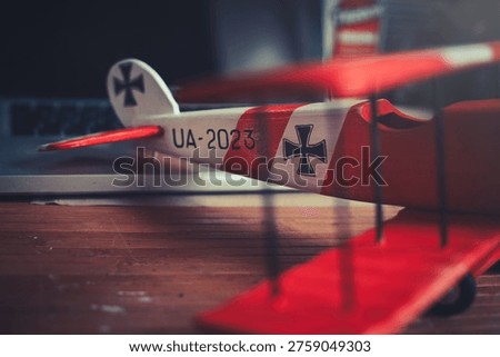 Horizontal close-up view of the tail section of a handcrafted red and white wooden triplane model, resting on a desk in a workshop.