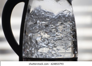 Horizontal closeup of water boiling in a glass vessel, with a light gray background with horizontal out-of-focus bands.
