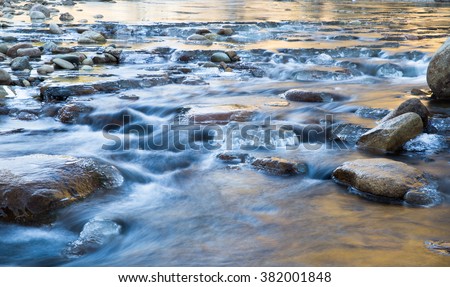 horizontal color image, taken with very slow shutter speed, showing water flowing in a creek in winter, with ice formations / Creek flowing in Winter with Rocks and Ice