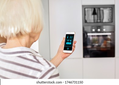 Horizontal Concept. Female Old Hands Holding Phone With App Smart Home Screen In Living Room Kitchen House. Touch Icon Manage System. Elderly Lady Control Lights With App. Safety Environment Interior