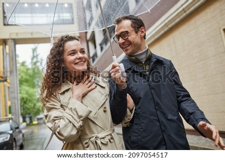 Horizontal dutch angle medium portrait of Caucasian man and woman enjoying time together outdoors walking under umbrella and talking