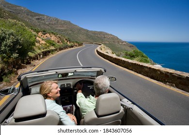 Horizontal elevated rear view of a joyous couple driving a convertible on a winding coastal highway on a sunny day with copy space. - Shutterstock ID 1843607056