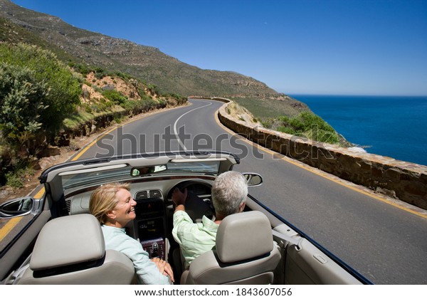 Horizontal elevated rear view of a joyous couple\
driving a convertible on a winding coastal highway on a sunny day\
with copy space.