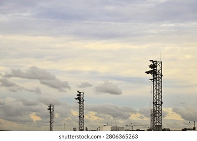 A horizontal eye-level shot of multiple high-mast airport floodlight towers rising into a cloudy overcast sky. The industrial lightning masts stand above the airfield infrastructure, providing extensive copy space in the sky area, ideal for aviation logistics and transport background graphics.