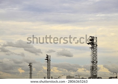 A horizontal eye-level shot of multiple high-mast airport floodlight towers rising into a cloudy overcast sky. The industrial lightning masts stand above the airfield infrastructure, providing extensive copy space in the sky area, ideal for aviation logistics and transport background graphics.