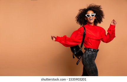 Horizontal Fashion  Image Of Excited Black Woman Jumping With Happy Face Expression On Beige Background. Wearing Vintage Red Shirt