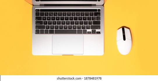 Horizontal flat lay minimalist photo with a silver grey laptop computer, and a wireless white-colored mouse on a yellow background.