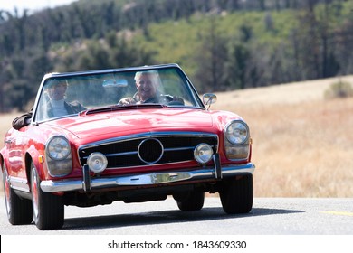 Horizontal front view of a senior couple on a road trip in a red convertible smiling at the camera on a sunny day with copy space.