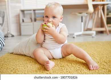 Horizontal Full Body Shot Of Baby Sitting On Carpet Biting And Eating Green Apple, Copy Space