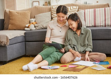 Horizontal Full Shot Of Two Cheerful Asian Girls Sitting On Floor Against Sofa Making Holiday Cards For Mothers Day, Copy Space