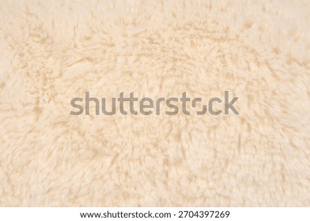 A horizontal full-frame close-up shot of a soft, dense, and textured beige or cream-colored artificial fur fabric