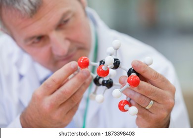 Captura horizontal de cabeza y hombro de un ingeniero químico que examina una estructura molecular con foco en la estructura en mano.