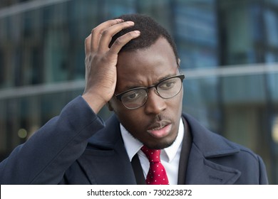 Horizontal headshot of young dark-skinned businessman standing outdoors with facepalm gesture, touching head with palm with puzzled and worried face expression