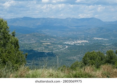 Horizontal high angle panoramic view of a vast valley with a town and distant mountain ranges under a cloudy sky in Spain.