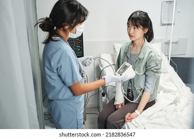 Horizontal High Angle View Shot Of Doctor Measuring Blood Pressure Of Young Asian Woman In Emergency Room