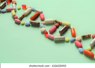 Horizontal image of a  collection of prescription capsules and tablets in the shape of DNA running diagonally across the picture on a light green background with room for copy (text).