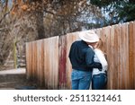 Horizontal image of a cowboy and cowgirl kissing up against a fence. The cowboy hat is blocking most of their faces. Romantic kiss between cowboy and cowgirl.