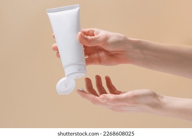 Horizontal image of female hands squeezing cream from a white blank tube. Concept of cosmetology and natural skin care product. Mockup for your design.