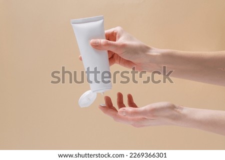 Horizontal image of female hands squeezing mockup face cream on finger on beige isolated background. Natural cosmetics for skin care concept.