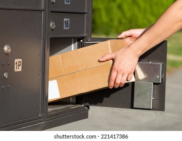 Horizontal Image Of Female Hands Taking Large Package Out Of Postal Mailbox With Green Grass And Sidewalk In Background 