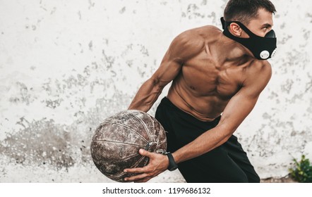 Horizontal Image Of Fitness Muscular Male Doing Exercises With Medicine Ball In Mask On Concrete Background Outdoor. Copy Space For Advertising. Shirtless Sportsman Doing Workout 