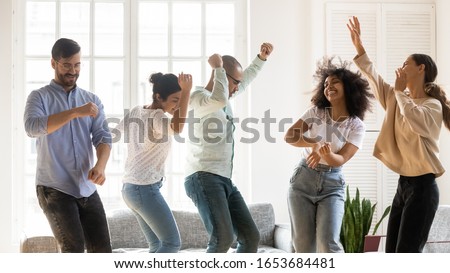 Horizontal image five active multinational cheerful best friends listening favourite track raised hands dancing spend time together moving in living room enjoy life weekend fooling around having fun