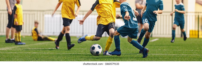 Horizontal Image Of Football Players Kicking Match. Boys In Soccer Duel. Kids In Two Football Teams Running After Classic Soccer Ball. Horizontal Sports Background. Legs Of Young Players On Football