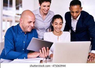 Horizontal Image Of Four Business People From Diverse Backgrounds, Of Multiethnic Complexion Unified By Working Together While Looking At A Laptop And Electronic Tablet.