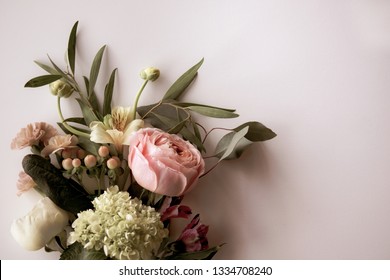 Horizontal image of fresh cut, pink and white flowers, buds, and berries with greenery on a pale pink background with copy space