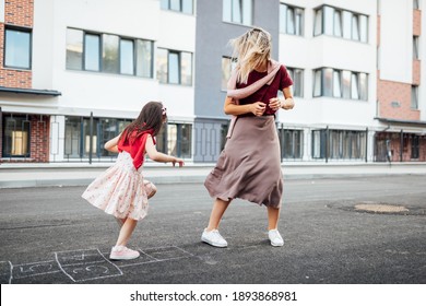 Horizontal Image Of A Little Girl Playing Hopscotch With Her Mother On A Playground Outside. A Happy Child Plays With Her Mom. Kid Plays With Mum Hopscotch Drawn On The Pavement.