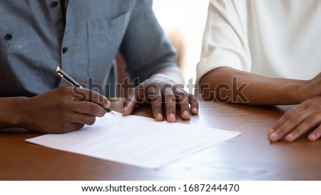 Horizontal image man holding pen put signature on agreement African couple filling form bank application taking loan, affirming rental contract, real estate purchasing, hands and table close up view Stockfoto © 