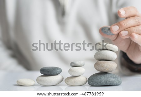 Horizontal image of a man stacking pebbles on a table with copyspace for text. Concept of risk management and wealth.