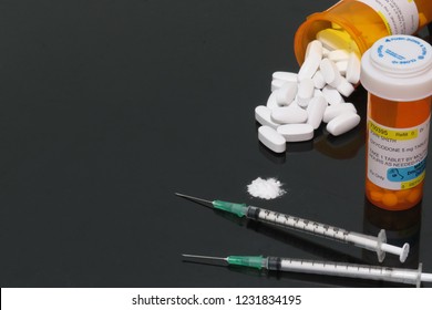 Horizontal image of narcotics (opioids.) Represented by a prescription bottle of oxycodone, hydrocodone tablets, syringes & fentanyl powder on a reflective black background (room for copy (text).
