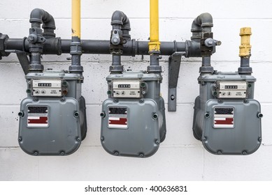 A horizontal image of natural gas meters hanging outside on a white wall of a building.