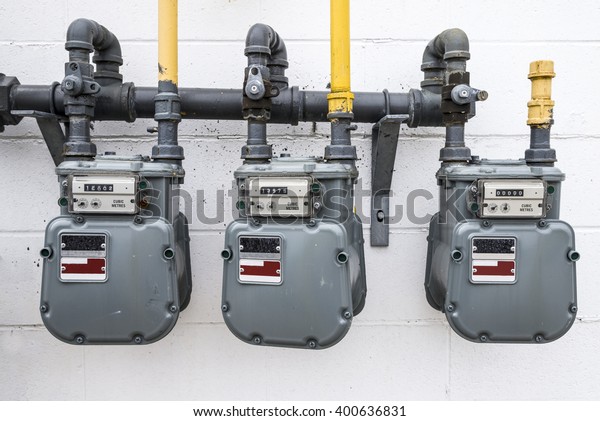 A horizontal image of natural gas\
meters hanging outside on a white wall of a\
building.
