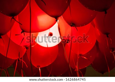 Horizontal image of red ballons with strings with one ballon lit white. Could represent red and white blood cells